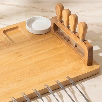 Close-up view of NovoBam bamboo charcuterie board detailing the upright magnetic block holding four wooden cheese knives, a ceramic dipping bowl, and stainless steel appetizer forks