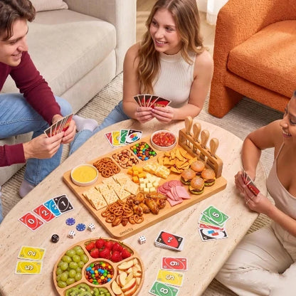 Friends playing a card board game around a living room coffee table enjoying snacks and sliders on a NovoBam bamboo charcuterie platter with round fruit tray