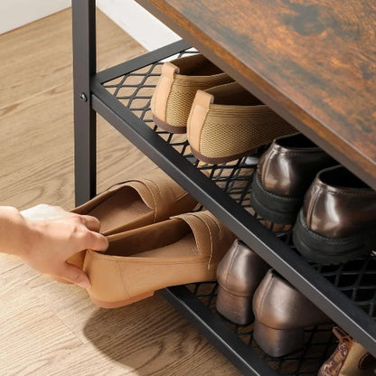 Person placing beige slip-on shoes onto the dense black metal mesh shelf of an industrial entryway shoe organizer bench.
