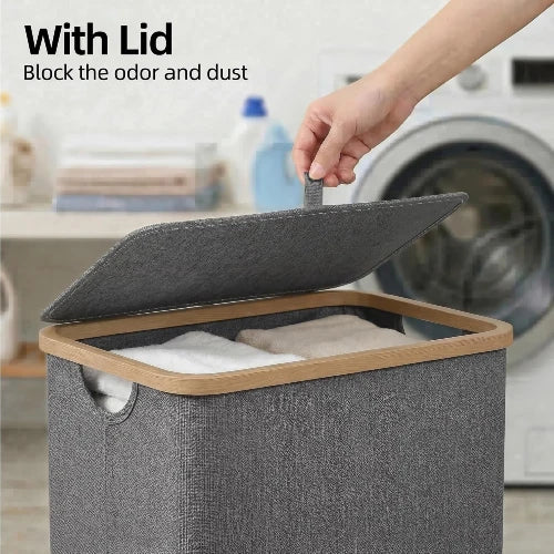 Close-up of hand lifting the hinged fabric lid of a gray slim laundry hamper with natural bamboo frame to contain odors and dust