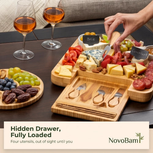 NovoBam square bamboo charcuterie board filled with artisan cheeses and meats featuring a slide-out drawer with utensils and companion fruit tray.