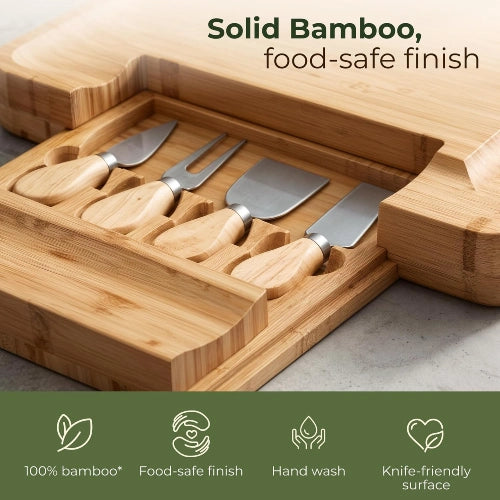 Close-up of solid bamboo charcuterie board slide-out drawer holding 4 stainless steel cheese knives with custom carved compartments.
