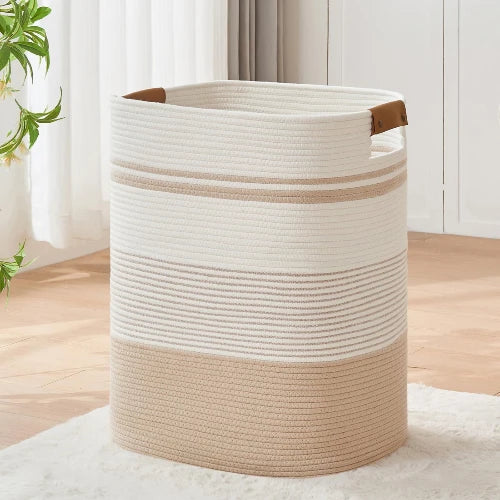 Tall rectangular woven cotton rope laundry hamper in off-white and tan with leather handles, standing upright in a modern home.