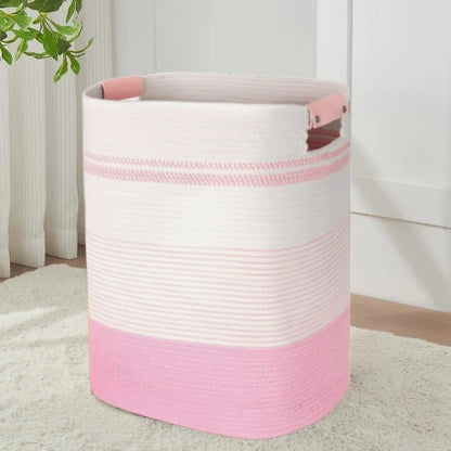 Tall rectangular woven cotton rope laundry hamper in pink and white stripes with pink handles, standing upright in a nursery room.